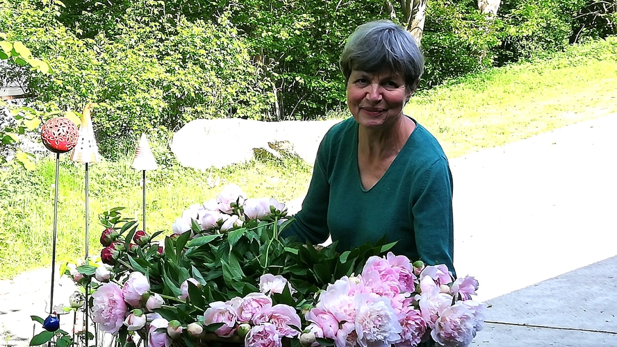 KI generiert: Eine Frau mit Blumenstrauß steht im Freien, von grüner Vegetation umgeben.