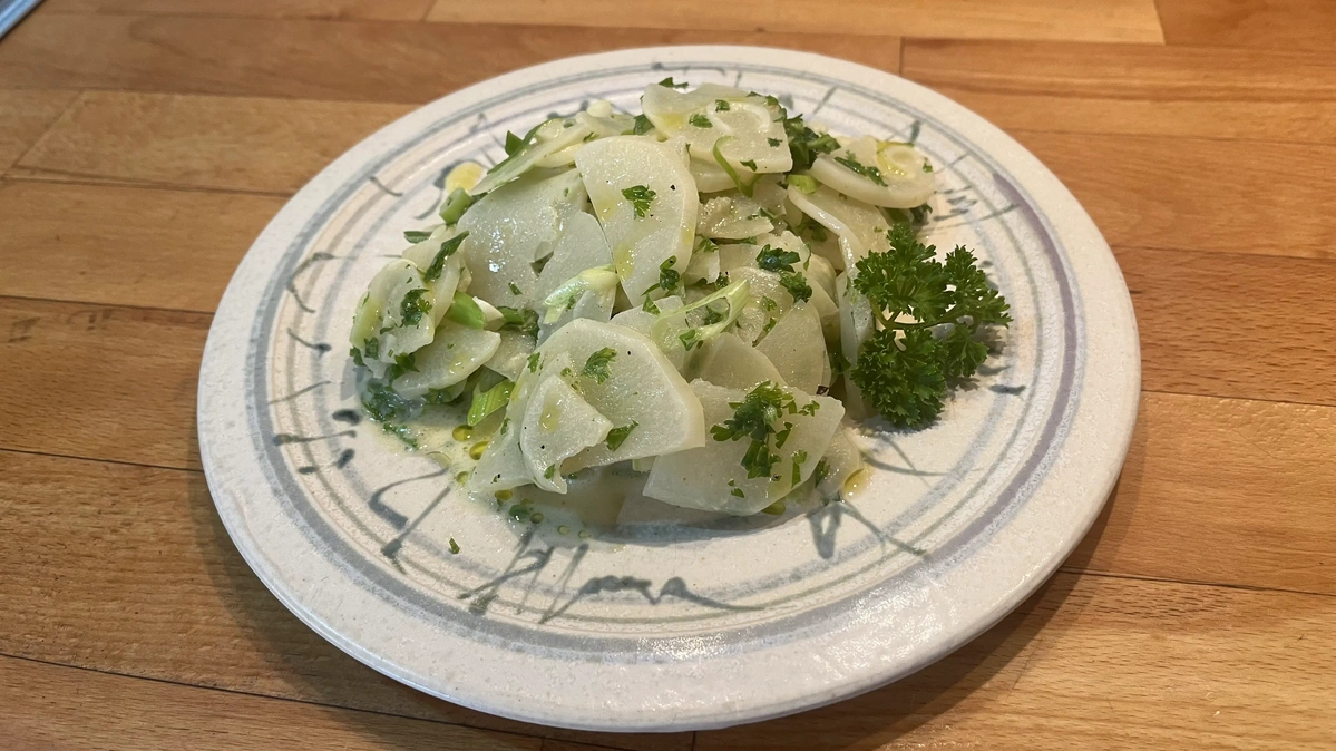 Gegarte Mairübchen mit Lauchzwiebeln und Petersilie auf bemaltem Keramikteller
