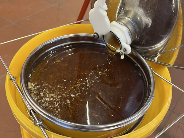Honig läuft aus der Schleuder durch zwei Siebe in einen Eimer