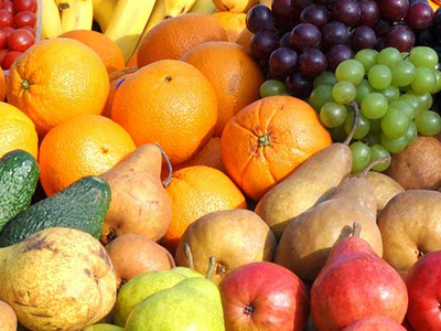 Verschiedene Früchte wie Bananen, Orangen, Trauben, Birnen, Avocado und Äpfel stapeln sich bunt zusammen.