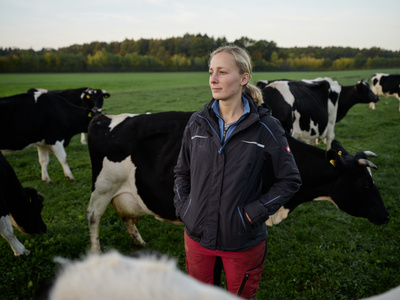 Eine junge Bäuerin steht mit ihren Milchkühen auf der Weide