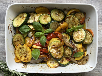 Ein Teller mit gebratenem Gemüse, darunter Zucchini und Paprika, garniert mit frischem Basilikum.