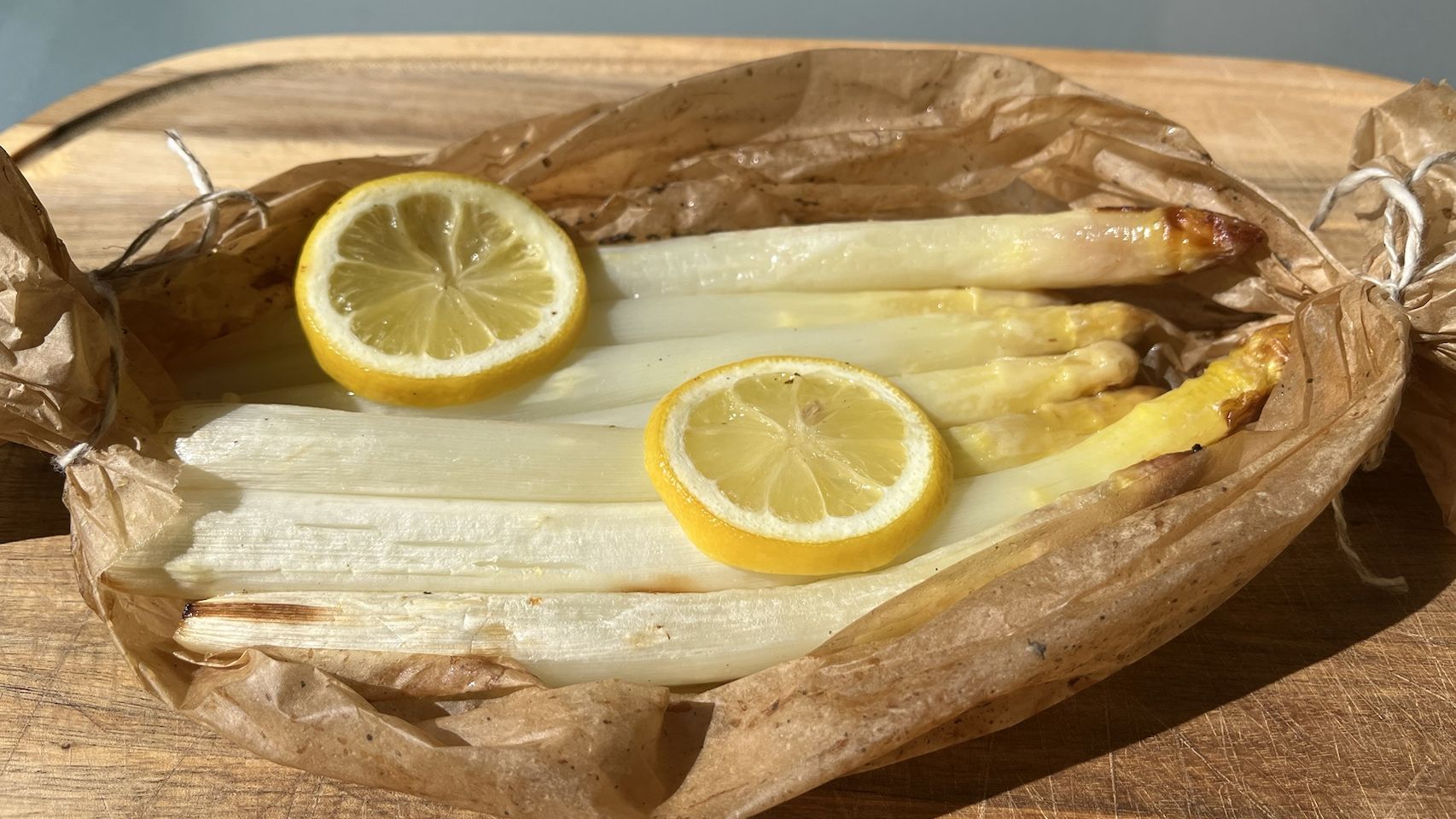 Weißer Spargel in Backpapier gegart, darauf zwei Scheiben Zitrone