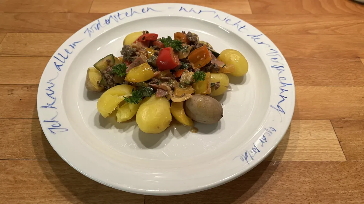 Weißer Teller mit blauer Aufschrift. Darauf kleine Kartoffeln und eine bunte Paprika-Hack-Pfanne