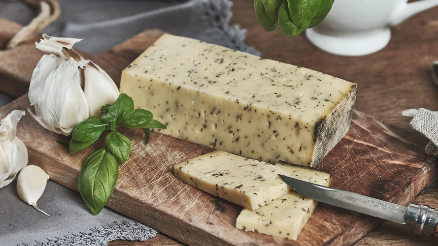 Ein rechteckiges Stück Kräuterkäse mit Knoblauch und Basilikum auf einem Holzbrett.