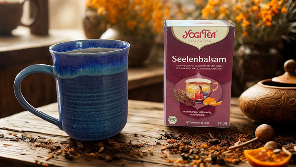 Eine blaue Tasse neben einer Yogi Tea "Seelenbalsam" Packung auf einem Holztisch.