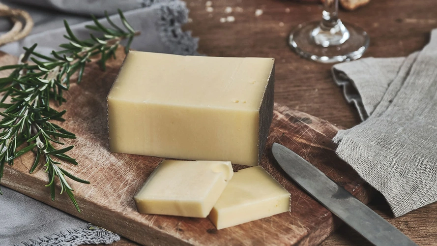 Ein Holzbrett mit Käse und Rosmarin, daneben ein Messer und ein Glas Wein.