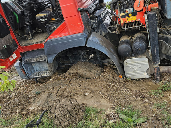 KI generiert: Ein roter LKW ist auf unebenem, schlammigem Boden festgefahren, wobei sein Rad tief im Erdreich steckt. Das Fahrerhaus des Fahrzeugs ist geöffnet und der Motorbereich ist sichtbar.