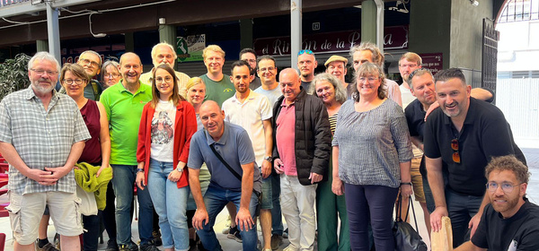 KI generiert: Eine Gruppe von Menschen posiert lächelnd für ein Foto in einem Innenraum oder überdachten Raum. Sie stehen dicht beieinander und scheinen eine freundliche Atmosphäre zu teilen.