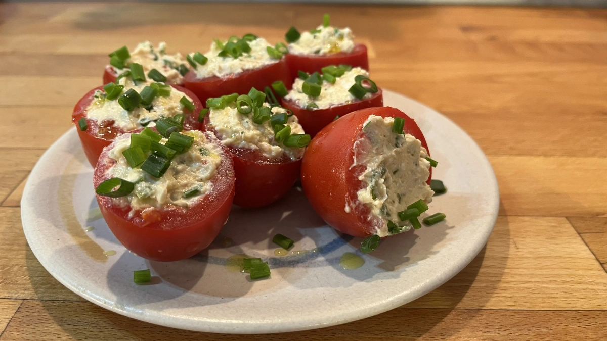 Gefüllte Tomaten mit einer cremigen Mischung, garniert mit Frühlingszwiebeln, auf einem Teller serviert.