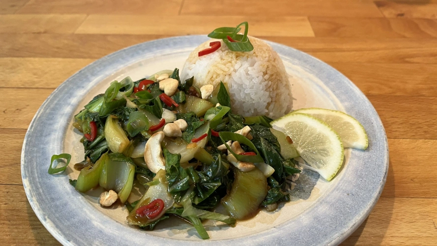 KI generiert: Ein Teller mit Reis, gebratenem Gemüse, Cashewkernen und Limettenscheiben.