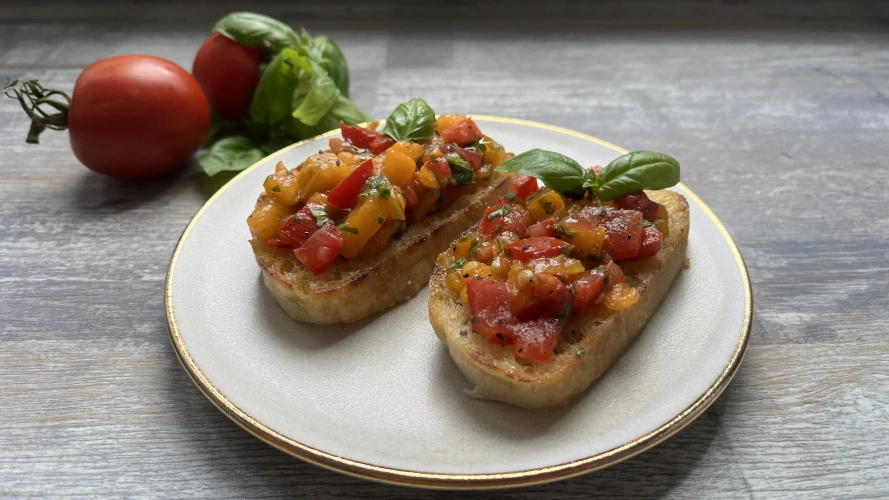 KI generiert: Zwei Bruschetta-Stücke mit Tomaten und Basilikum auf einem Teller, frische Tomaten und Basilikum im Hintergrund.