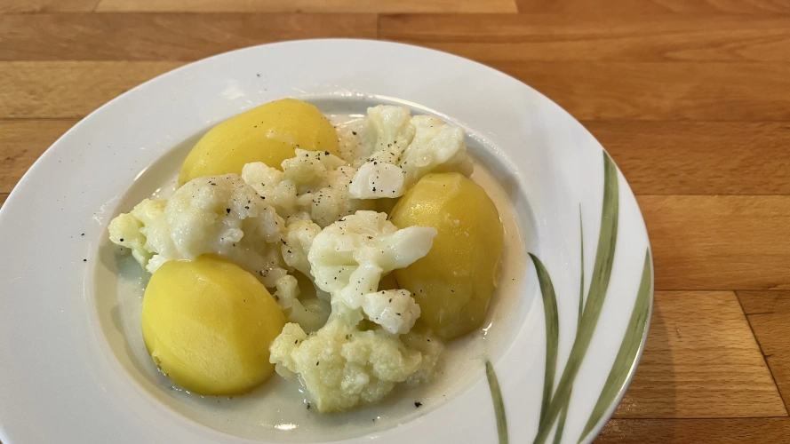 KI generiert: Ein Teller mit Kartoffeln und Blumenkohl in heller Sauce auf einem Holztisch.