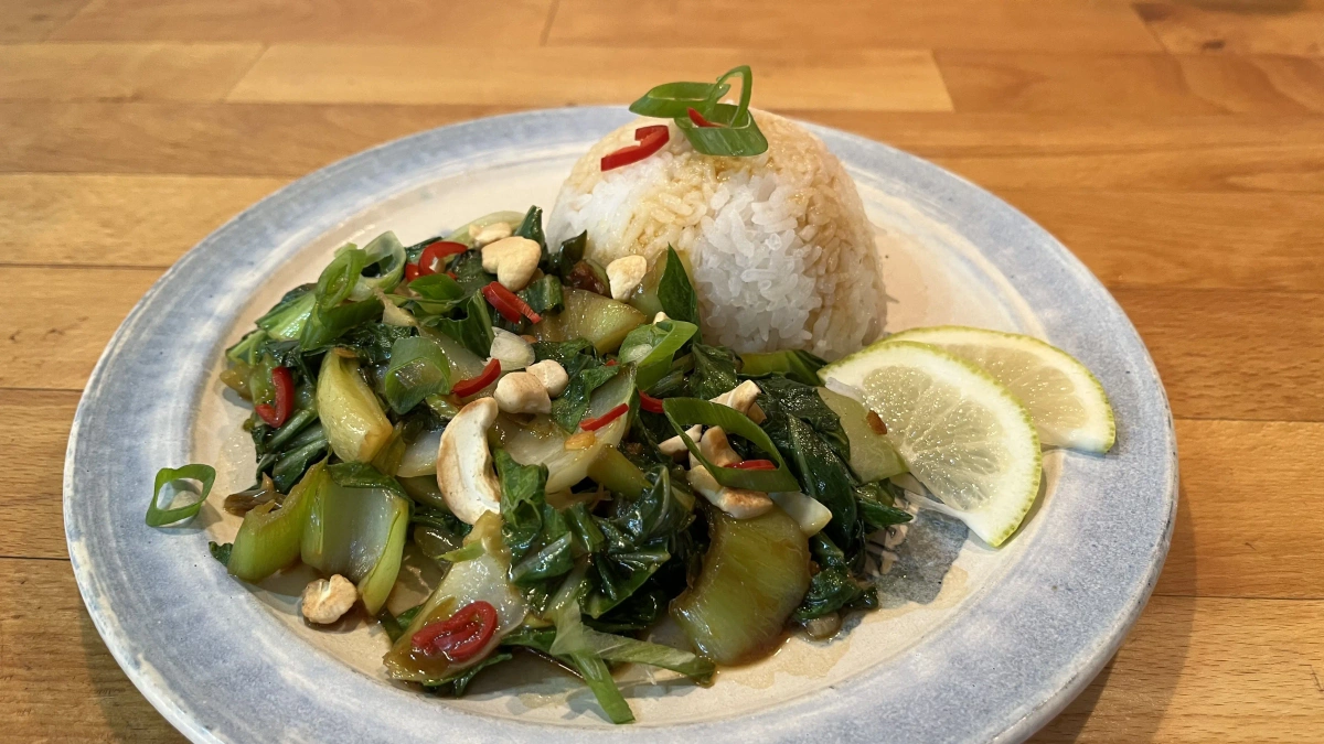 Ein Teller mit gebratenem Gemüse, Reis und Limettenscheiben, dekoriert mit Nüssen und Chili.