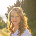 Eine Frau im Freien bei Sonnenuntergang, sie trägt ein weißes Oberteil.