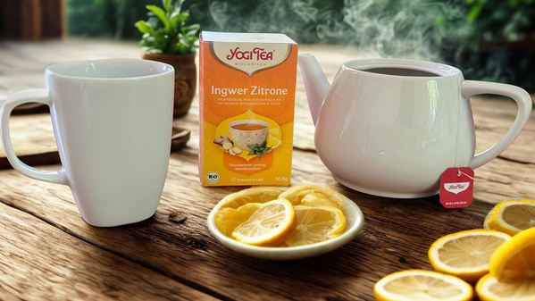 Eine Teekanne und Tasse mit "Yogi Tea Ingwer Zitrone", Zitronenscheiben im Vordergrund.