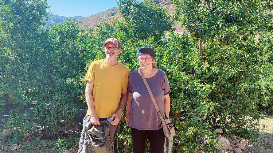 KI generiert: Das Bild zeigt zwei Personen, die vor grünen Bäumen im Freien stehen. Sie lächeln und tragen Freizeitkleidung.