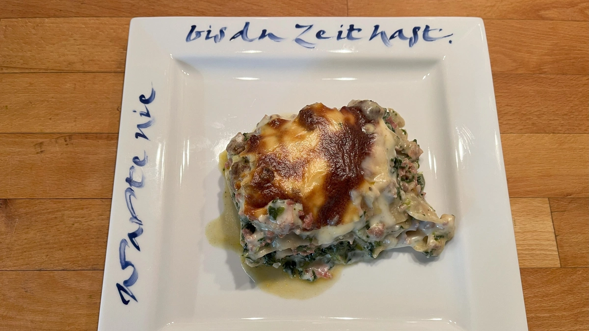 Spinatlasagne mit Hackfleisch auf weißem Teller mit blauer Aufschrift
