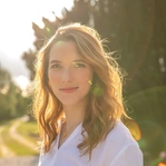 Eine Frau im Sonnenlicht lächelt draußen in einer natürlichen Umgebung.