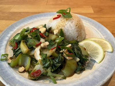 Reisgericht mit gebratenem Gemüse, Nüssen und Limettenscheiben auf einem Teller.