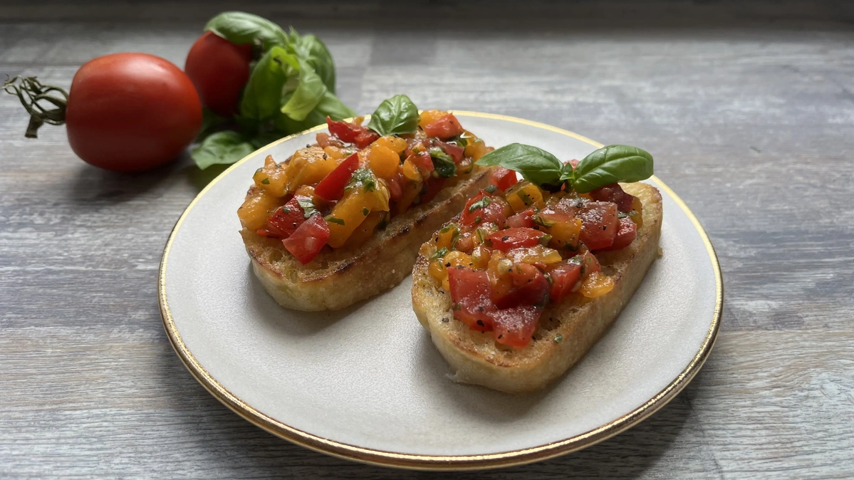 Zwei Bruschetta mit Tomaten und Basilikum auf einem Teller, Dekoration mit frischen Tomaten und Basilikum.