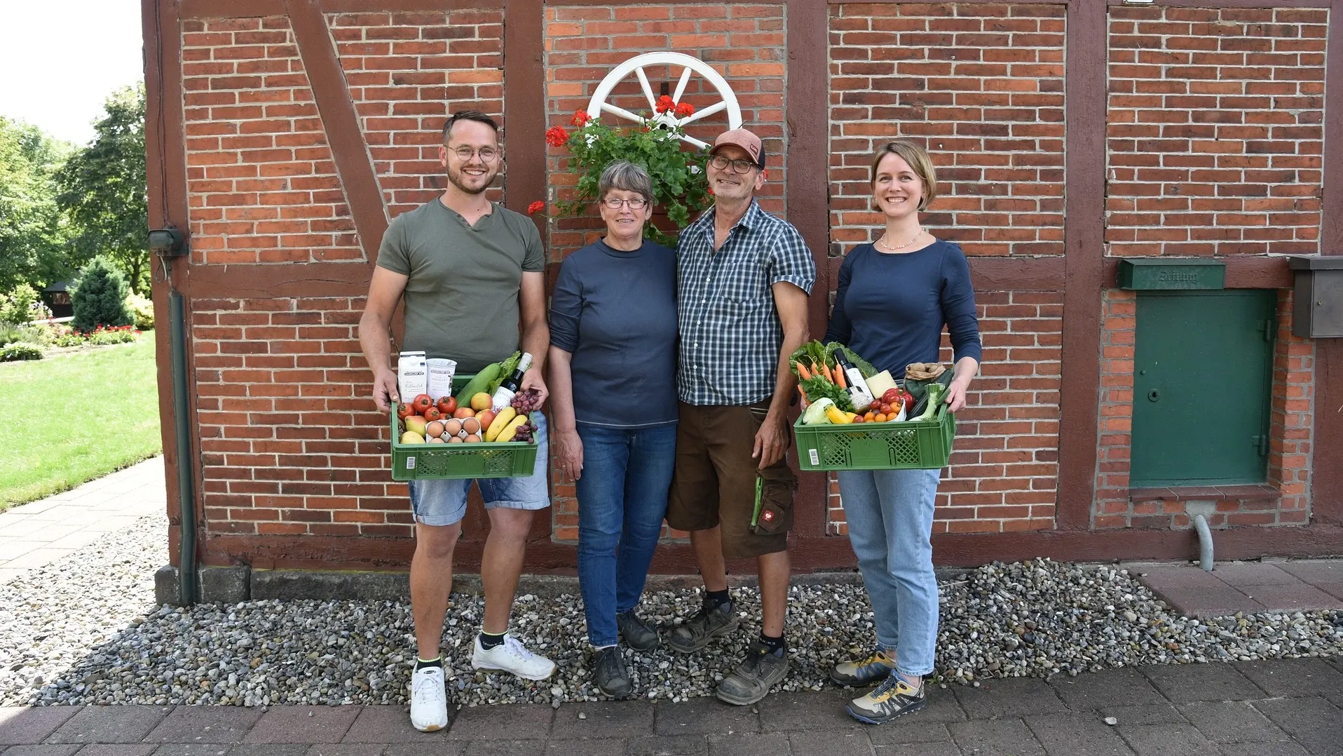 Hjalmar, Hedda, Jörg und Hjördis vor einem Fachwerkhaus mit gefüllten Biokisten