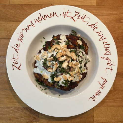 Ganzer marinierter Blumenkohl mit Joghurt-Petersilien-Cashew-Topping auf beschriftetem Teller