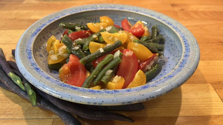 KI generiert: Salat mit grünen Bohnen und bunten Tomaten in einer blauen Schüssel auf einem Holztisch serviert.