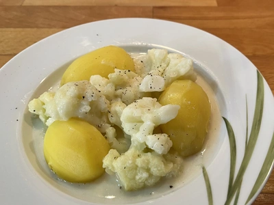 Ein Teller mit Kartoffeln und Blumenkohl in heller Soße, gewürzt mit Pfeffer.
