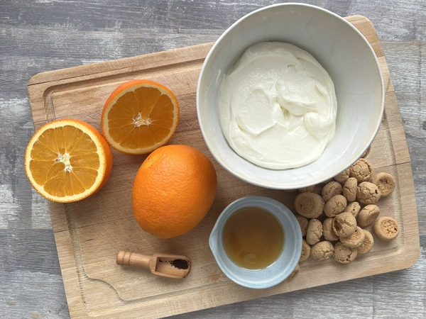 Orangen, Quark, Amarettini und Gewürze auf Holzbrett