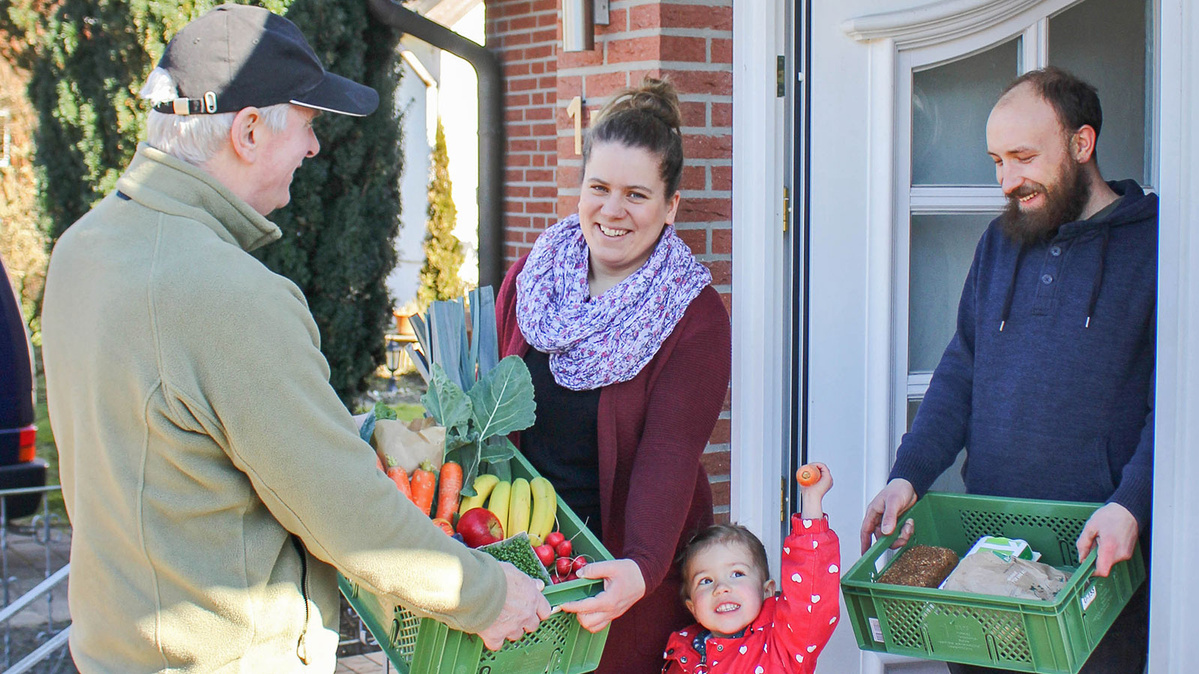Ein Lieferbote bringt Biokisten zu einer jungen Familie