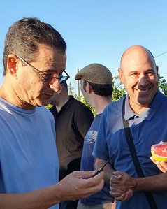 KI generiert: Das Bild zeigt eine Gruppe von Menschen im Freien, von denen einer eine aufgeschnittene Frucht, vermutlich eine Grapefruit, in der Hand hält. Die Stimmung wirkt freundlich und entspannt, während sie miteinander interagieren.