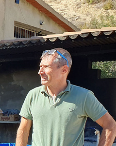 KI generiert: Ein Mann steht draußen neben einem blauen Fass vor einem Gebäude. Er trägt eine Sonnenbrille und schaut zur Seite.