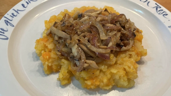 Steckrübenstampf mit Zwiebeln und Pilzen auf weißem Teller mit blauer Aufschrift