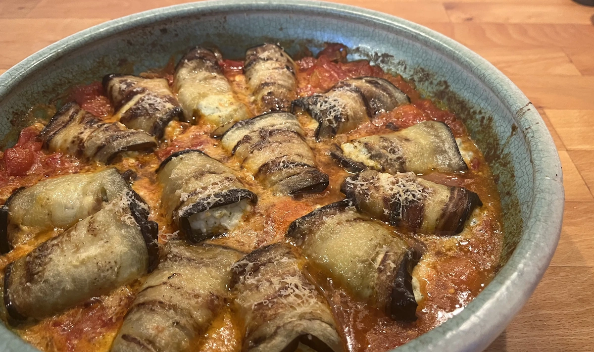 KI generiert: Ofengericht mit gefüllten Auberginenröllchen in Tomatensauce und geriebenem Käse in einer blauen Auflaufform.