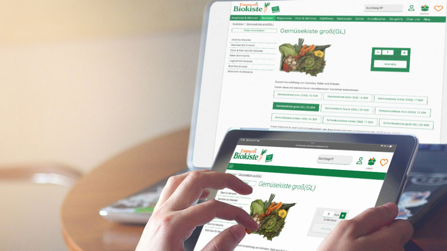 Hand zieht auf Tablet etwas auf | Im Hintergrund ein Laptop mit der gleichen Website