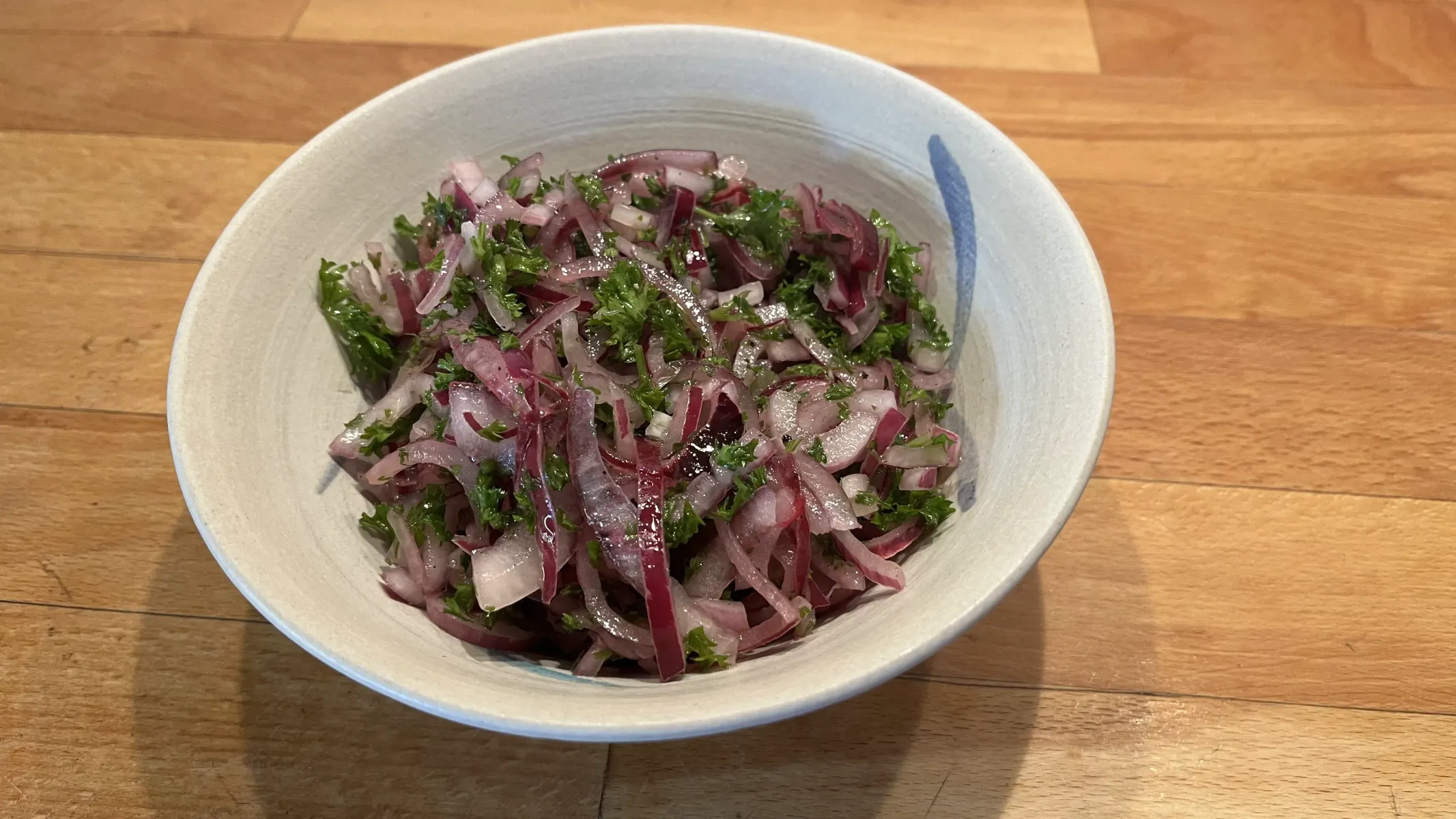 Salat aus roten Zwiebeln mit viel grüner Petersilie in einer Keramikschale