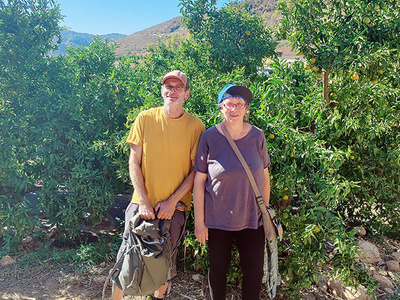 Zwei Personen posieren vor grünen Büschen in einer ländlichen Umgebung.
