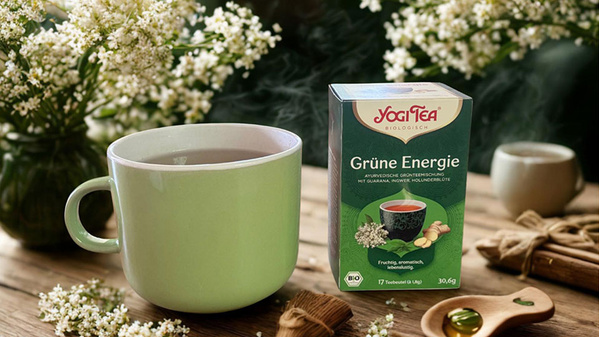 Eine Tasse Tee und eine Packung Yogi Tea "Grüne Energie" auf einem Tisch mit Blumen.
