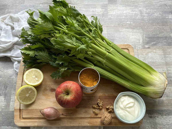 Stangensellerie, Zitrone, Apfel, Walnüsse und Gewürze auf Schneidebrett aus Holz
