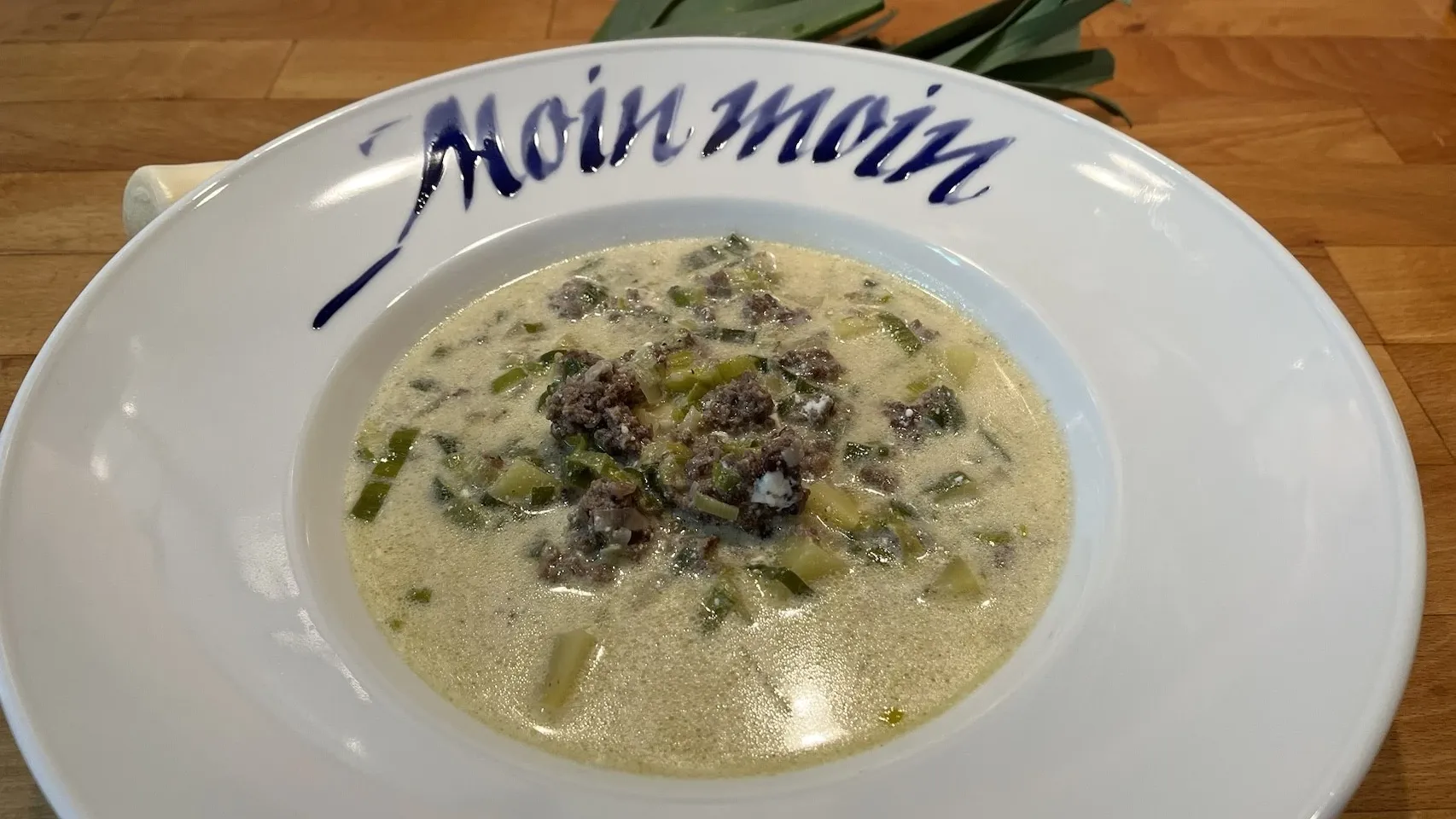 Käse-Lauch Suppe mit Hackfleisch in weißem Teller mit der Aufschrift "Moin Moin"