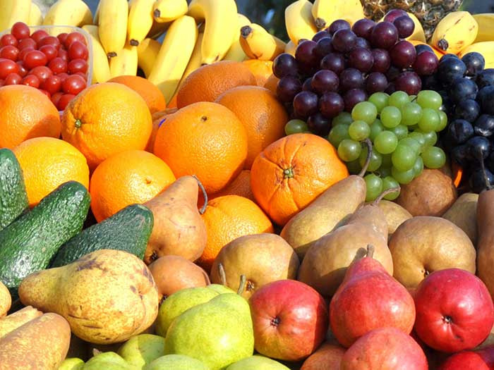 Eine Auswahl von Obst und Gemüse liegt schön platziert in einer hell ausgeleuchteten Auslage. Zu sehen sind Tomaten Bananen Orangen, Weintrauben, Birnen und Äpfel in verschiedenen Farben.