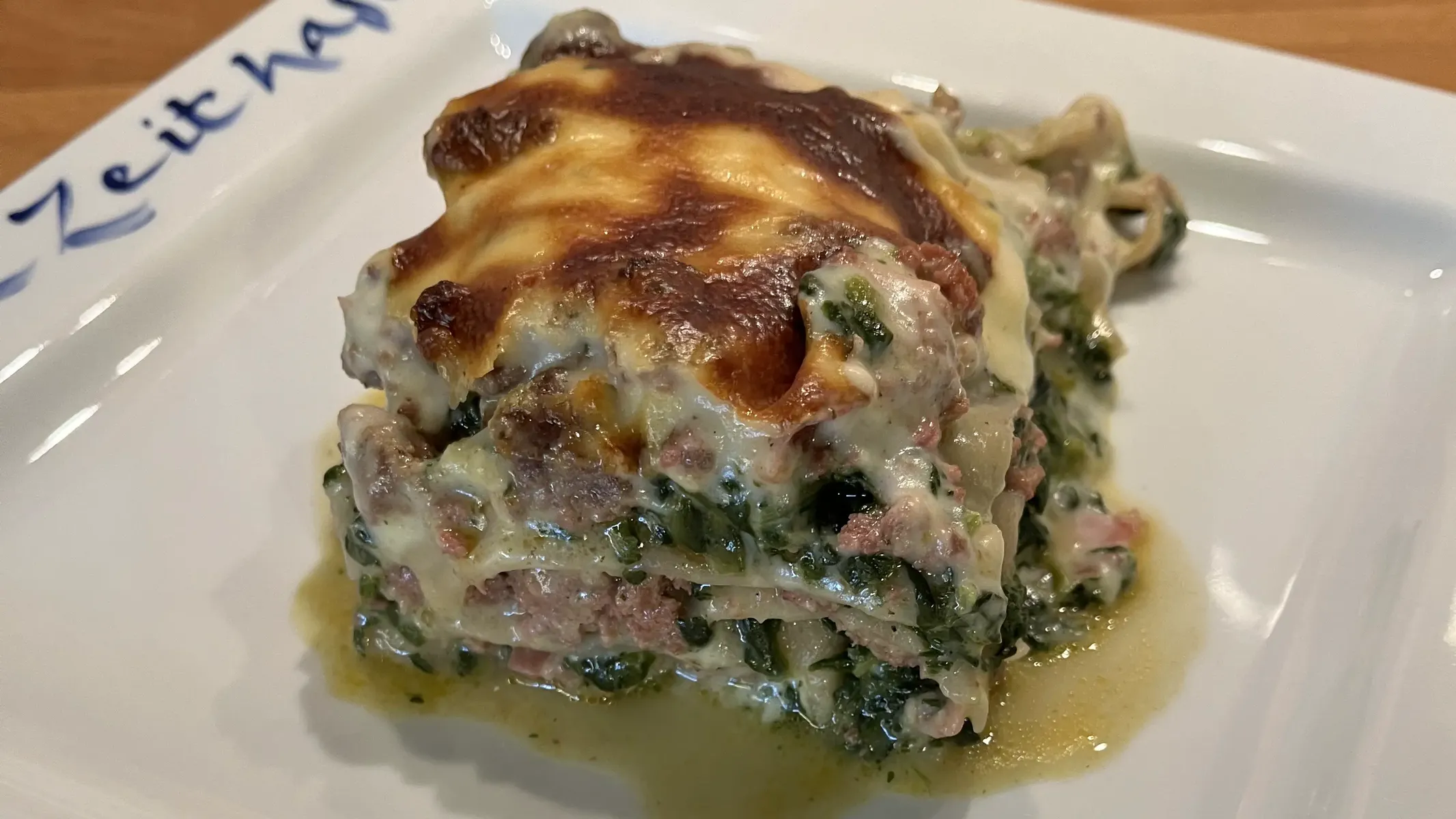 Spinatlasagne mit Hackfleisch auf weißem Teller mit blauer Aufschrift