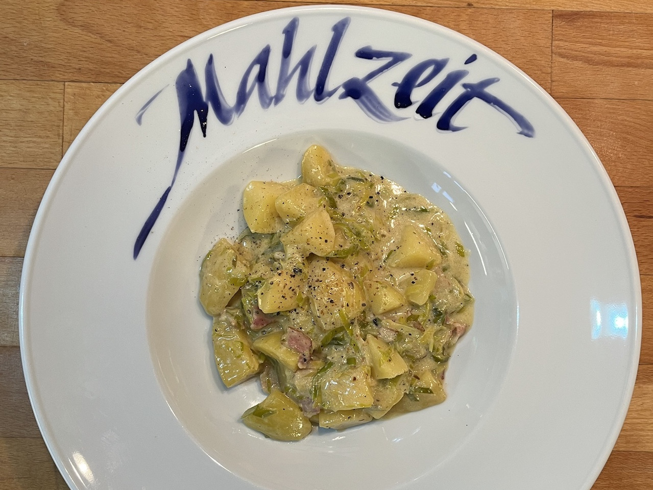 Gericht aus Kartoffeln und Lauch auf weißem Teller mit der Aufschrift "Mahlzeit"