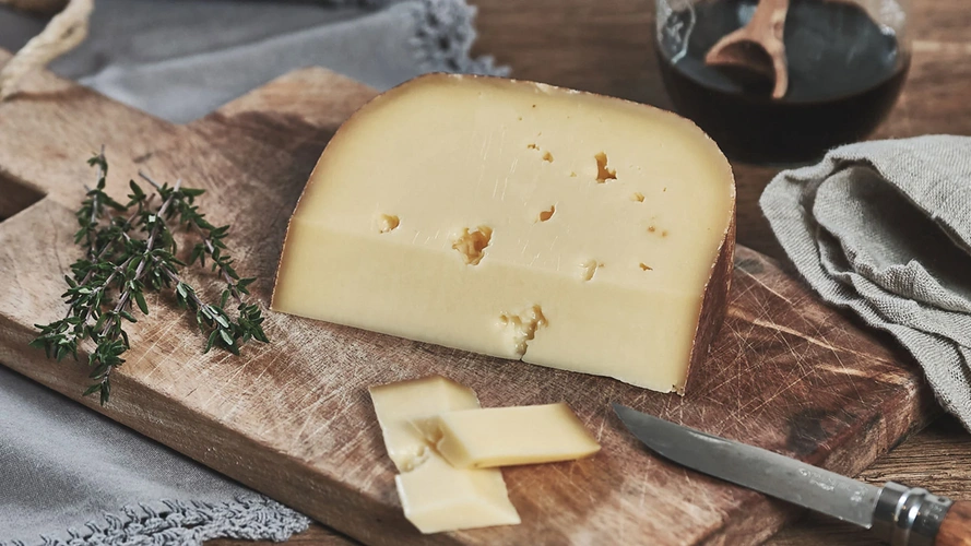 Ein Stück Käse auf einem Holzbrett mit Kräutern und einem Messer.