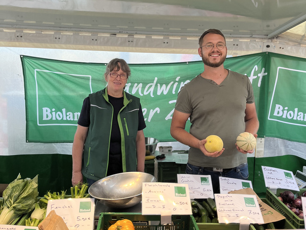 Hedda und Hjalmar hinter einem Marktstand mit Biolandgemüse