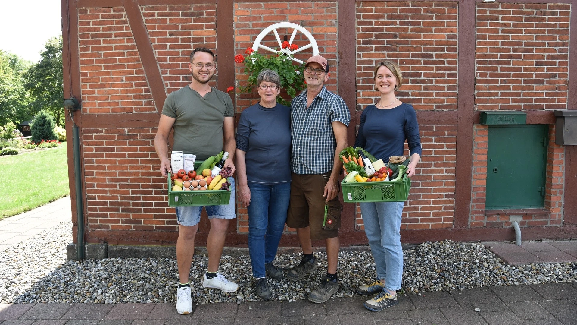 Hjalmar, Hedda, Jörg und Hjördis vor einem Fachwerkhaus mit gefüllten Biokisten